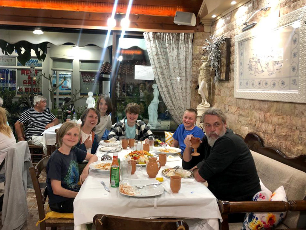 Foto von der Konfi-Freitzeit auf Kreta. Das Foto zeigt die Gruppe, bestehend aus Pastor Frank Bonkowski und den Konfis Hannes, Paale, Thies, Jost und Jannis am Tisch eines örtlichen Restaurants.