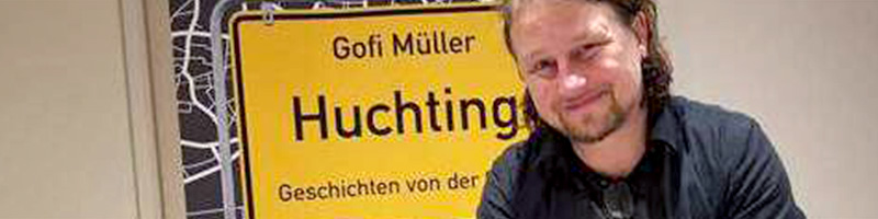 Header "Lesung Gofi Müller - Huchtingen": Autor Gofi Müller lächelnd vor einem Roll-up seines neuen Buches.